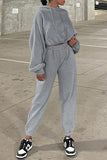 Person wearing a gray tracksuit with black and white sneakers on a concrete surface.