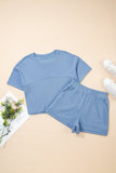 Blue crop top and shorts set on a beige surface with white sneakers and a plant.