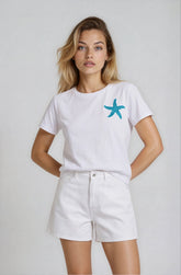 Woman wearing a white t-shirt with a blue starfish design and white shorts on a plain background