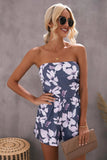 Woman in strapless navy floral romper with black sunglasses and beige clutch.