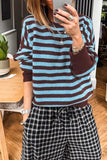 Person taking a mirror selfie in a blue and brown striped sweater and dark plaid drawstring pants.