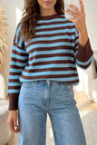 Woman taking a mirror selfie in a brown and light blue striped sweater with jeans.