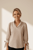 Woman wearing a striped blouse with tied sleeves against a neutral background