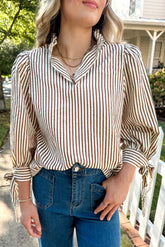 Woman wearing a striped blouse and blue jeans standing outdoors.