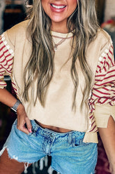Woman wearing a beige top with red sleeves and denim shorts, smiling.