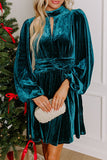 Woman in skobeloff teal velvet keyhole mock neck mini dress with a beaded clutch