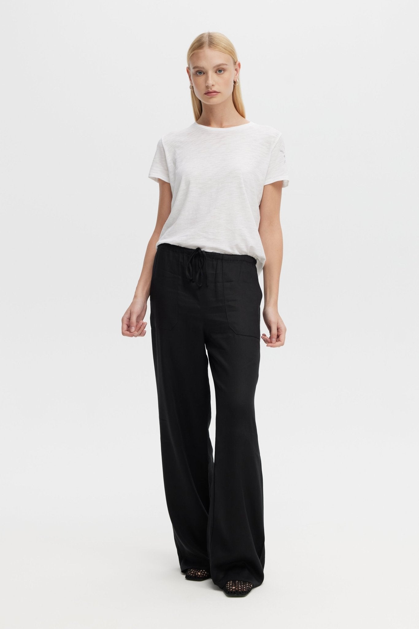 Woman wearing a white t-shirt and black wide-leg pants on a white background