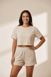 Woman wearing a beige crop top and shorts set against a plain background