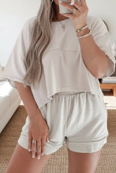 Person wearing a white outfit with shorts, holding a phone indoors.