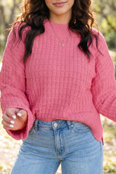 Woman in pink textured knit sweater with bell sleeves and light blue jeans.