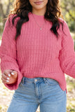 Woman in pink textured knit sweater with bell sleeves and light blue jeans.