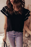 Person wearing a black top with ruffled sleeves and light blue jeans indoors.