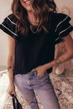 Woman wearing a black top with white trim and blue jeans, standing on a patterned rug.