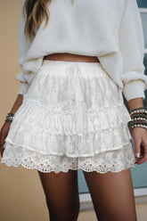 White lace skirt worn with a white sweater against a neutral background