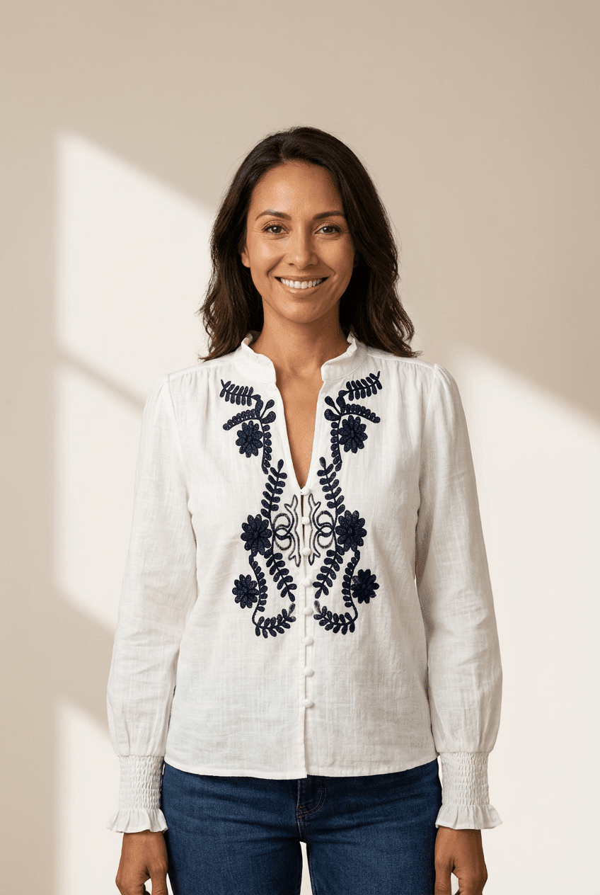 Woman wearing a white blouse with black embroidery against a beige background