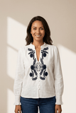 Woman wearing a white blouse with black embroidery against a beige background