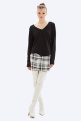 Woman wearing a black long-sleeve top, plaid skirt, and white knee-high boots on a white background