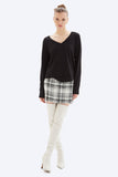 Woman wearing a black long-sleeve top, plaid skirt, and white knee-high boots on a white background
