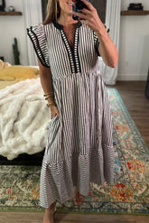 Woman taking a mirror selfie wearing a black and white striped dress in a room with a colorful rug.