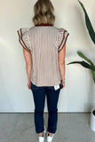 Woman wearing a striped shirt with ruffled sleeves against a white wall.