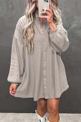 Person wearing a gray button-up dress against a dark background