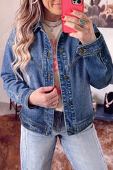 Woman taking a mirror selfie in a blue denim jacket, graphic T-shirt, and light-wash jeans