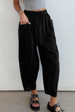 Person wearing black wide-leg pants and a gray top against a white wall.
