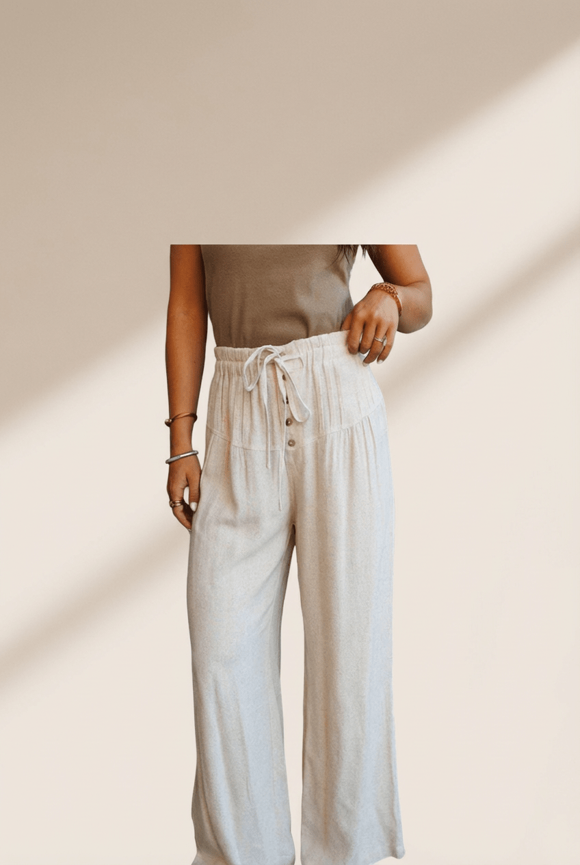 Person wearing a beige top and white pants against a neutral background