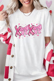 Person wearing a white shirt with pink text and hearts, holding a pink heart-shaped object.