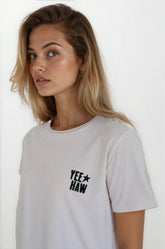 Woman wearing a white t-shirt with 'YEE HAW' text and star design on a plain background