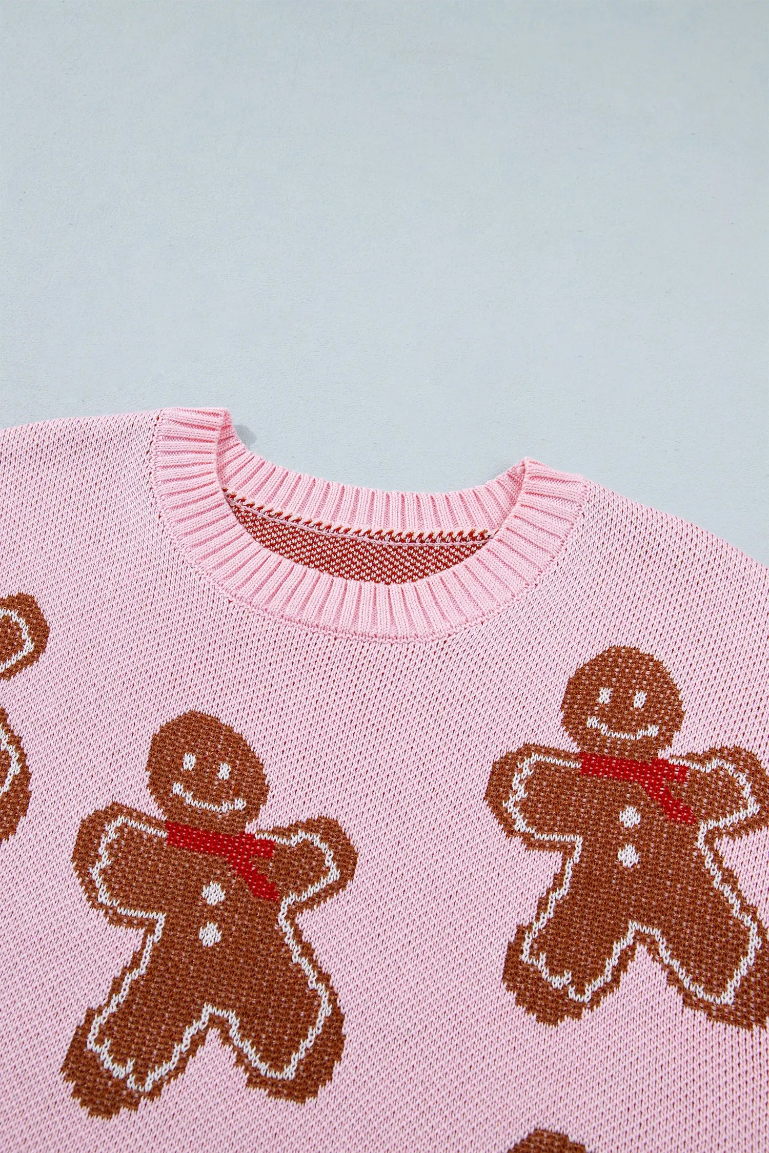 Close-up of pink knit sweater with brown gingerbread men, red scarves, and white details against light gray.
