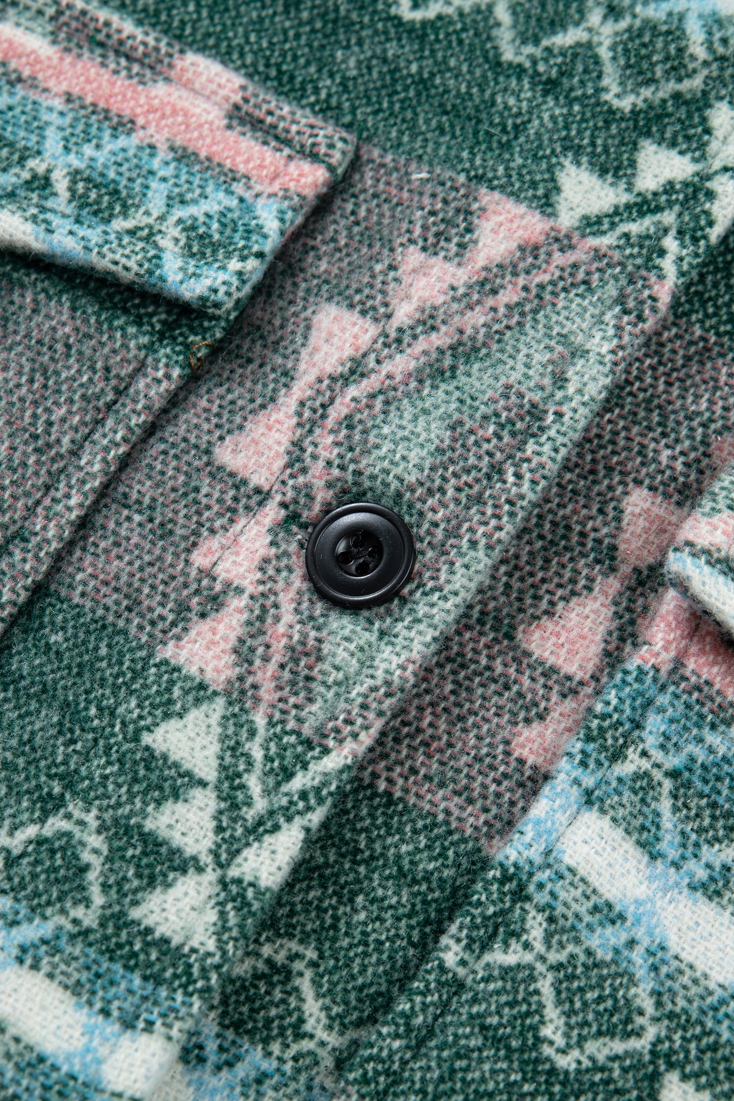 Close-up of a patterned fabric with a black button, showing a mix of green, pink, and white geometric and tribal-inspired designs.