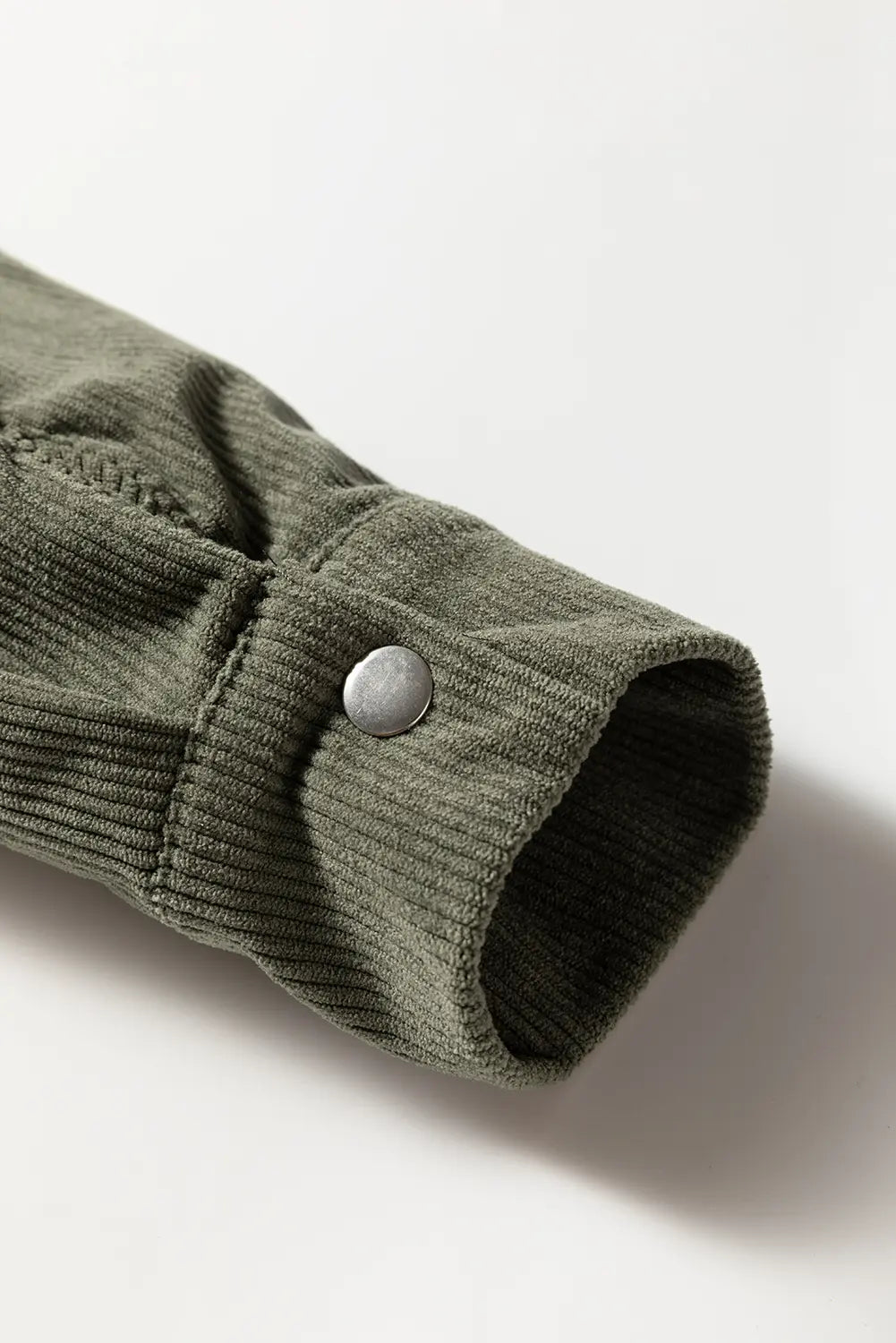 Close-up of a green corduroy jacket sleeve with a button on a white background