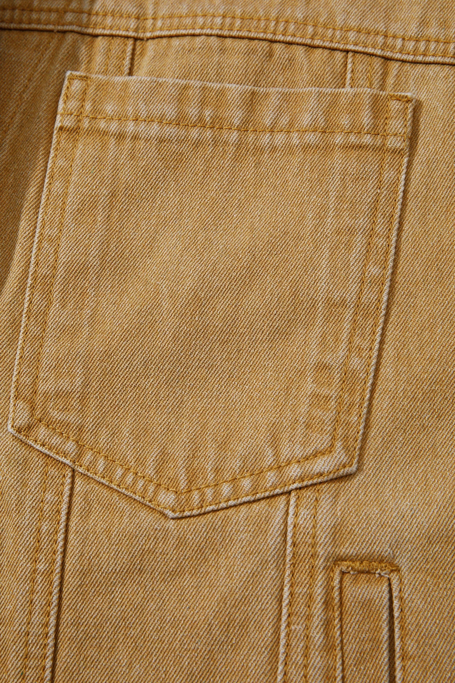 Close-up of a tan denim jacket showing a front patch pocket with detailed stitching and a textured twill weave.
