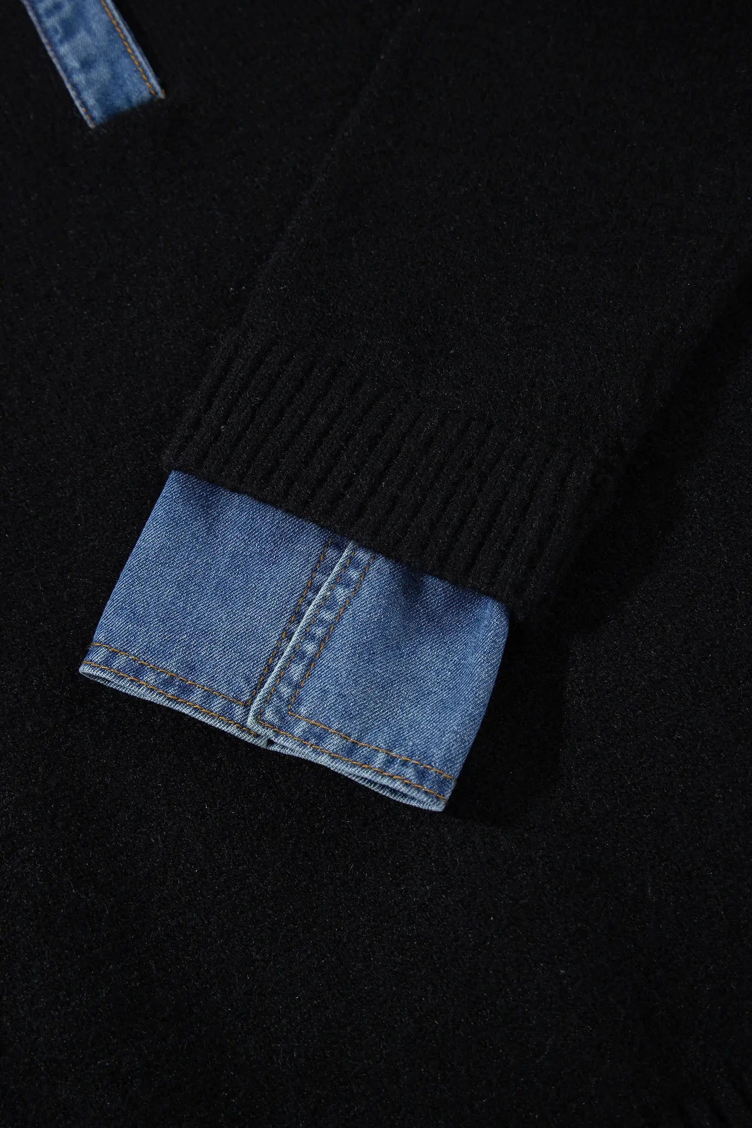 Close-up detail of a black knit garment with a ribbed cuff revealing a light blue denim lining.