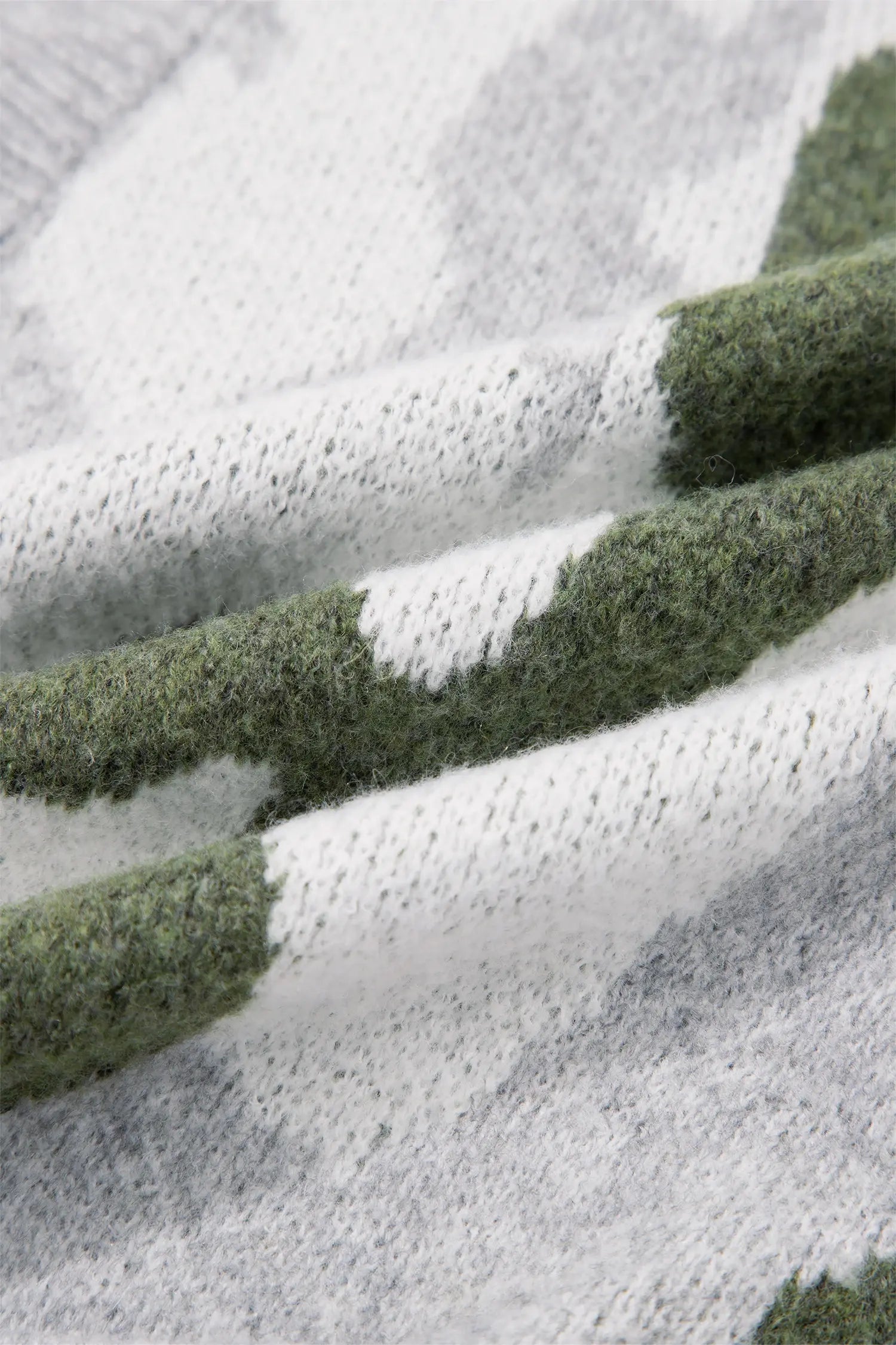 Close-up of a soft knit fabric with a repeating pattern of textured olive green and light gray blocks on a white base.