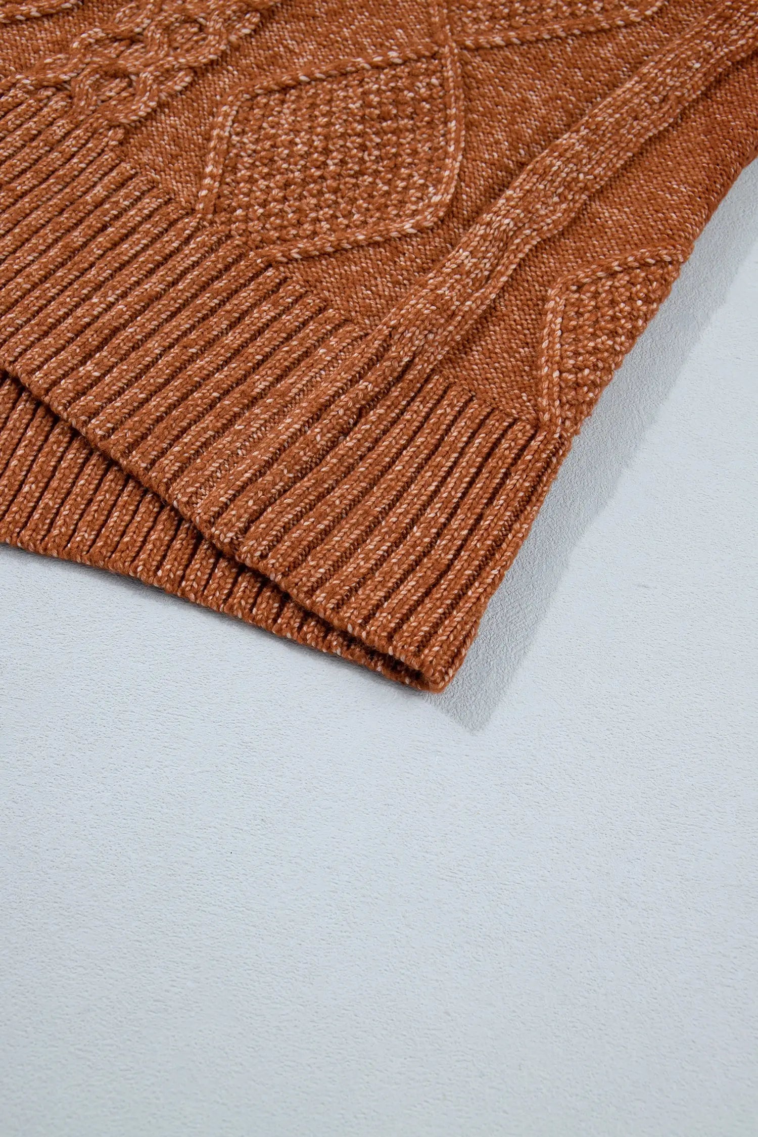 Close-up of rust-orange ribbed cuff corner on textured knit garment against light gray background.