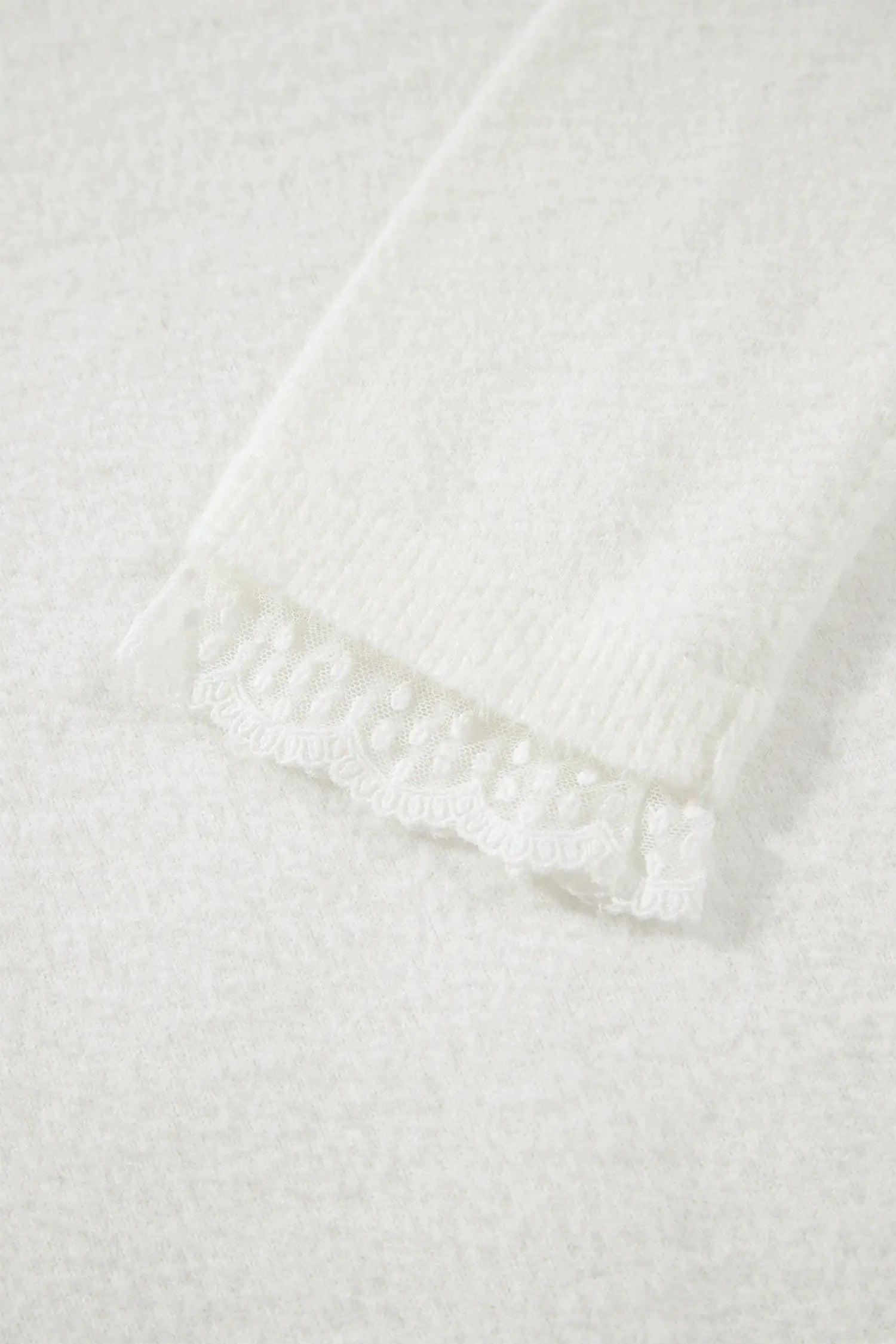 Close-up of a white knit fabric with a delicate white lace trim along the edge.