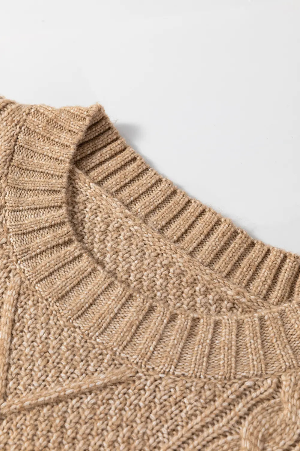 Close-up of a beige knitted fabric with a textured pattern on a light gray background