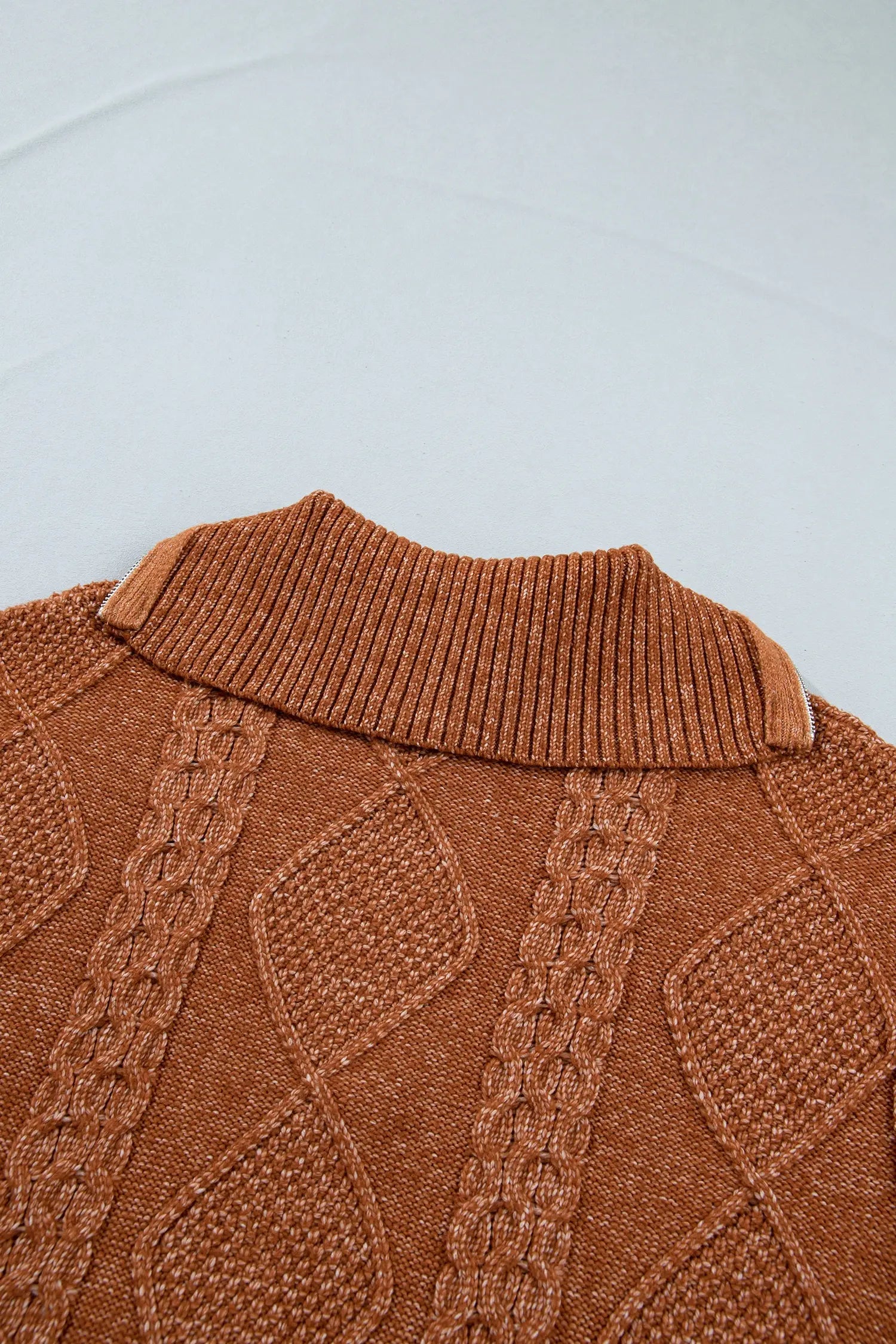 Close-up of ribbed brown knit sweater collar with textured cable-knit panels on light gray background.