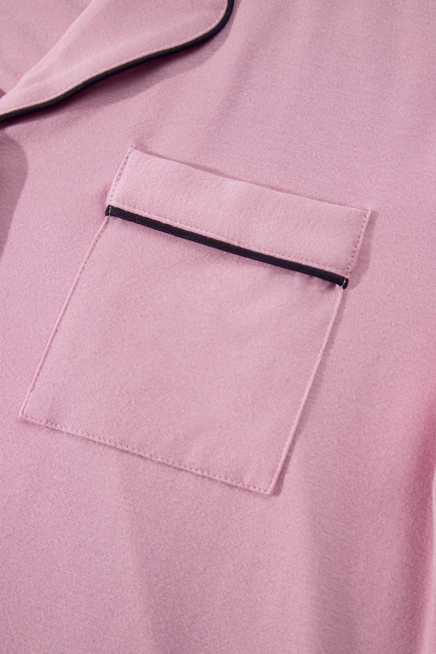 Close-up of a pink fabric garment with a chest pocket and thin black piping trim.