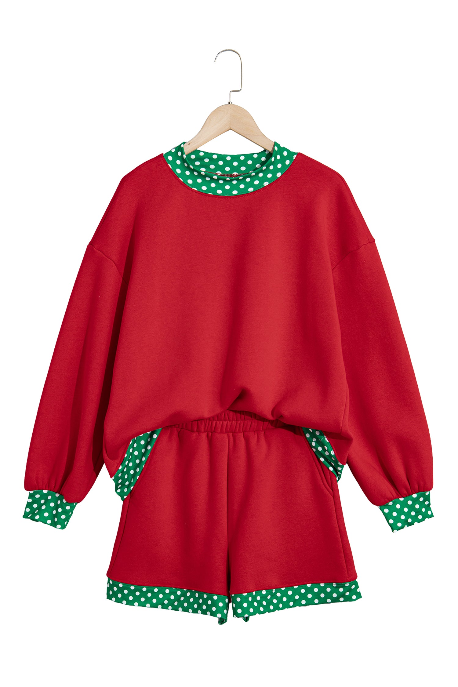 A red two-piece lounge set consisting of a long-sleeve sweatshirt and matching shorts, featuring green and white polka-dot trim on the collar, cuffs, and hem, hanging on a wooden hanger against a white background.