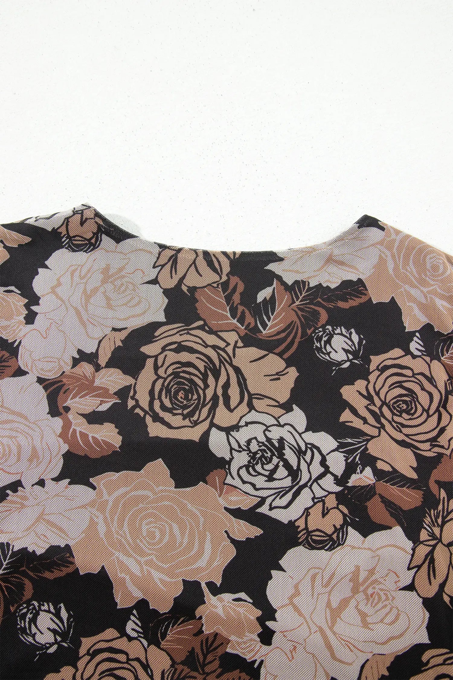A close-up of a floral-patterned top or dress featuring large roses in beige, cream, and brown tones on a black background, photographed against a plain white backdrop.