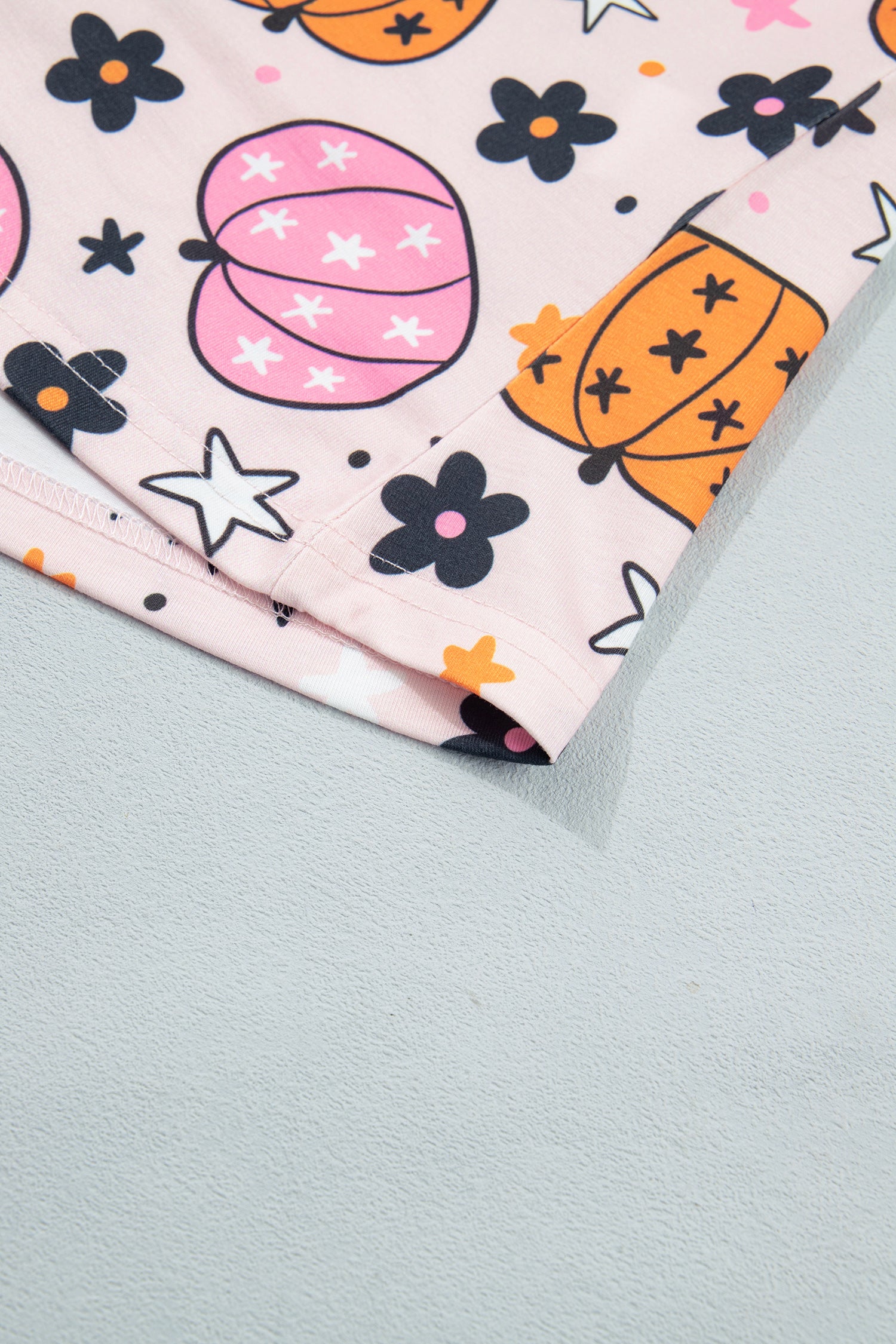Close-up of pink fabric with pumpkins, black flowers, and white stars.