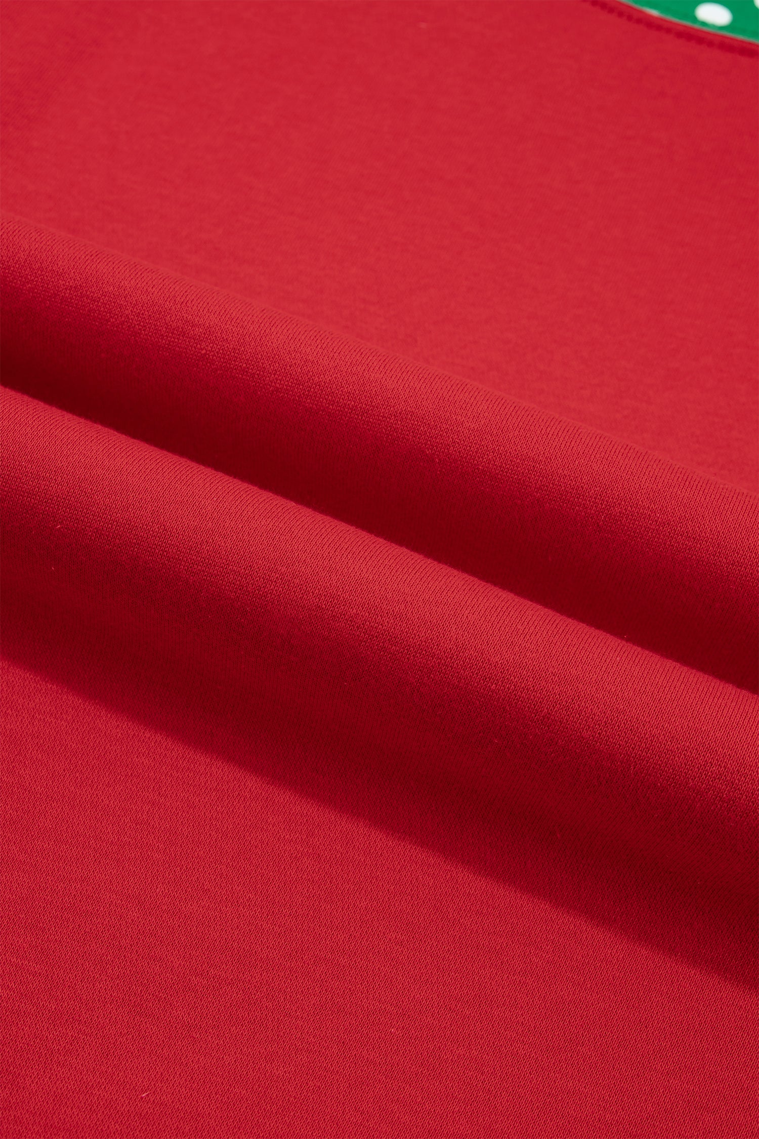 A close-up of a bright red fabric surface with soft folds and a small sliver of green and white visible at the top edge.