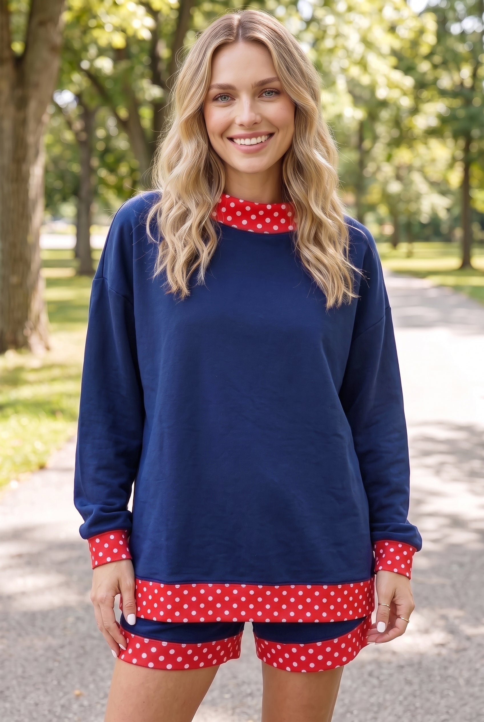 Woman wearing navy blue long-sleeve top and matching shorts with red-white polka-dot trim on a park path.