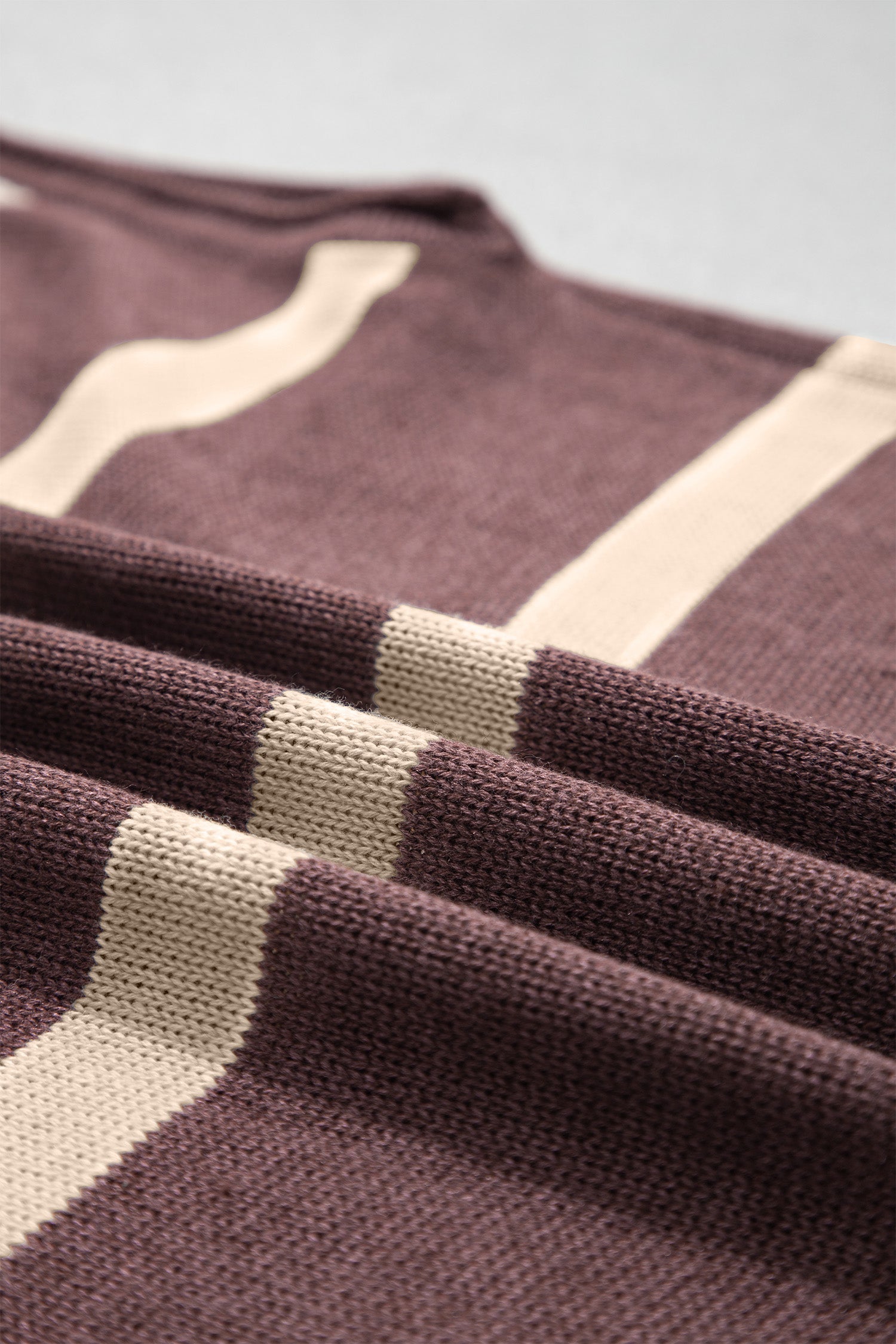 Close-up of a knit fabric with a dark brown base and cream-colored horizontal stripes, showing the detailed knit texture and folds.