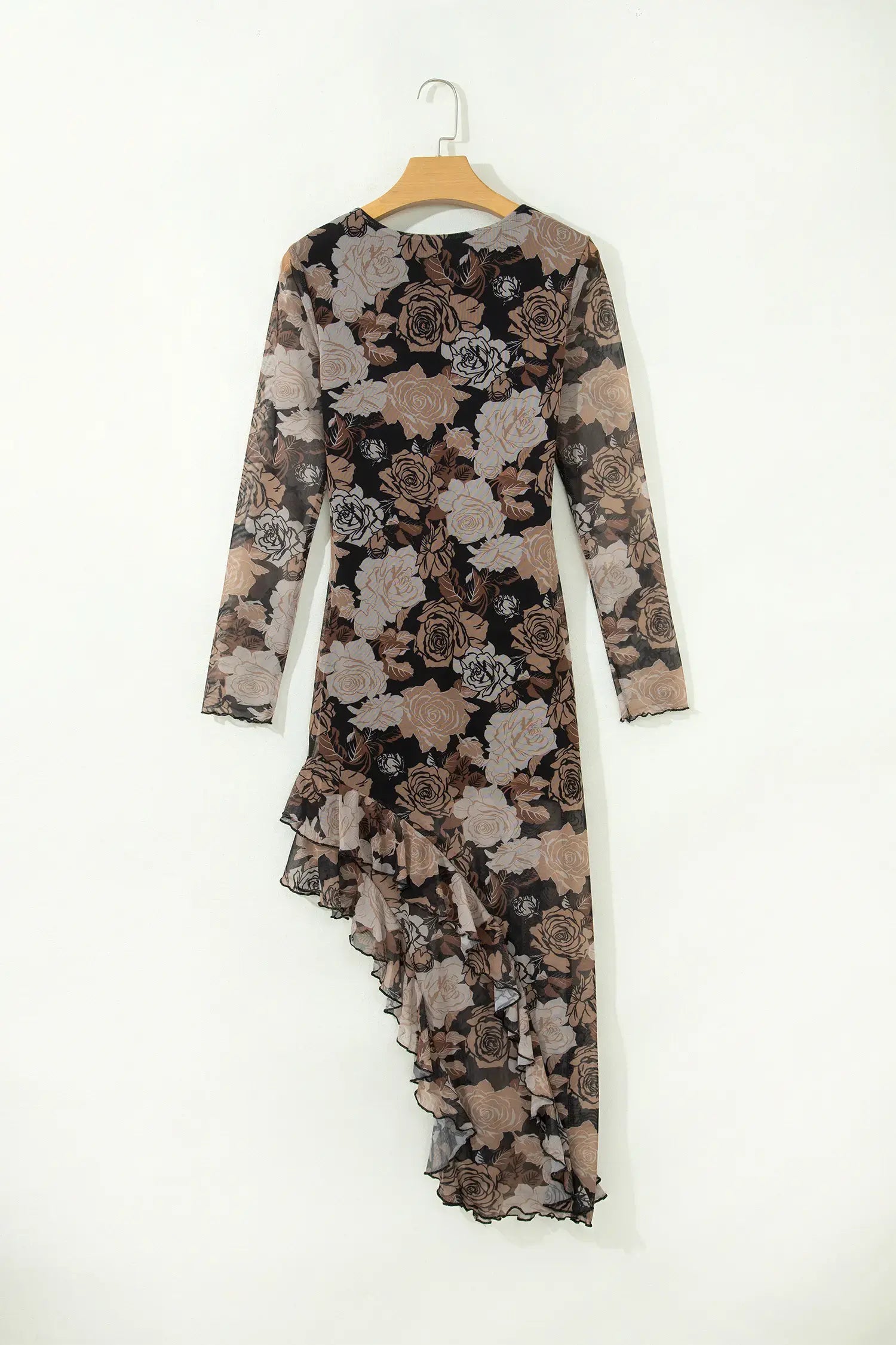 A long-sleeve midi dress with an asymmetrical ruffled hem, featuring a black, brown, and beige floral pattern, hanging on a wooden hanger against a plain white wall.