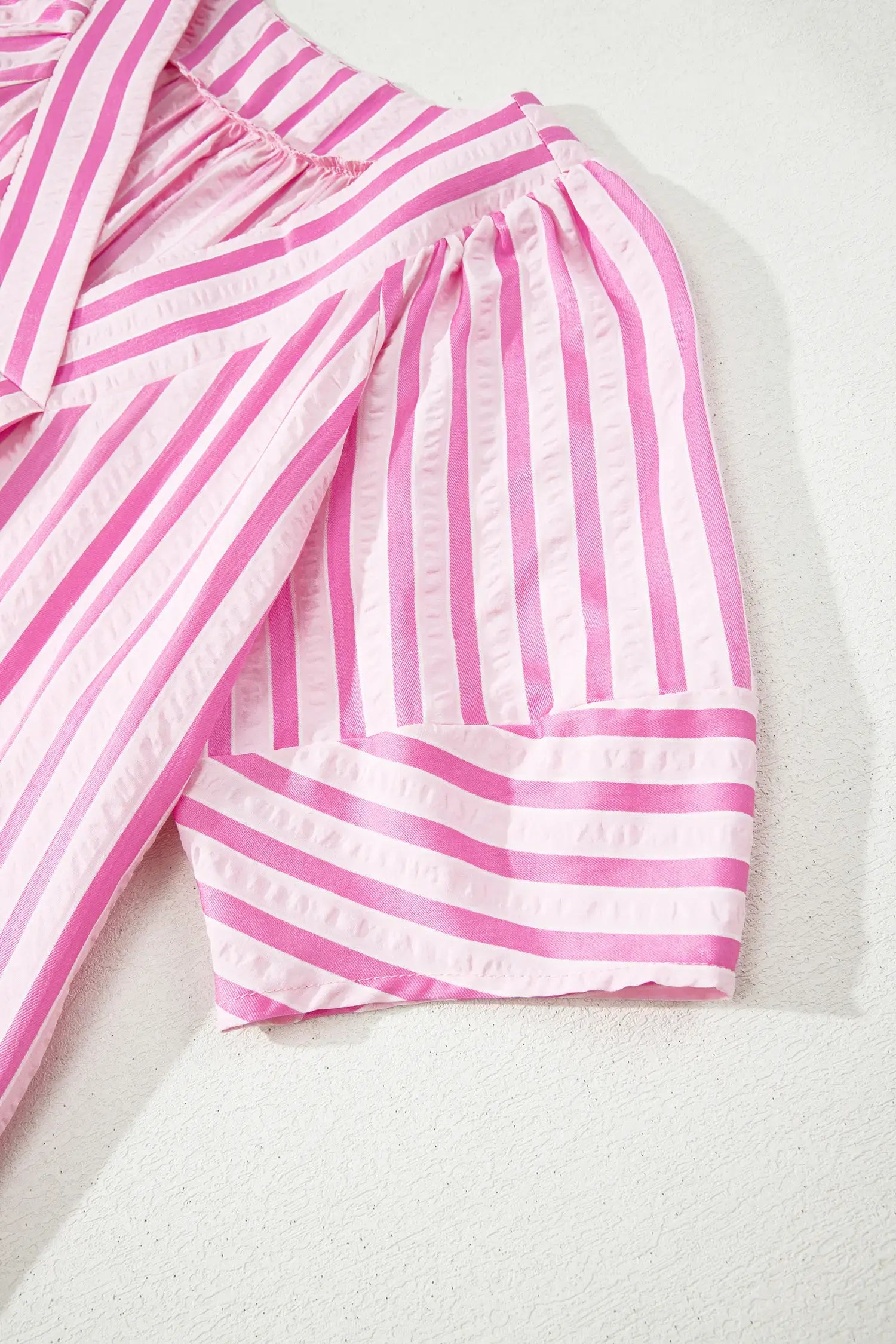 Pink and white striped fabric garment detail, showing gathered sleeves and a ruffled sleeve cuff on a light textured background.