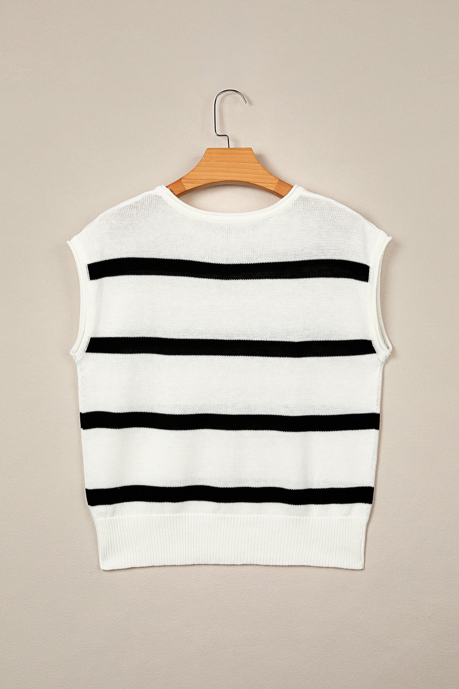 A sleeveless white knit sweater vest with horizontal black stripes, hanging on a wooden hanger against a solid beige background.